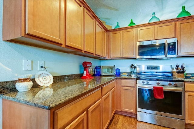 kitchen with dark stone counters, light wood-type flooring, and appliances with stainless steel finishes