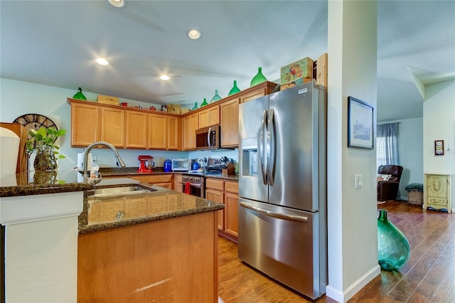 kitchen with sink, kitchen peninsula, dark stone countertops, wood-type flooring, and appliances with stainless steel finishes