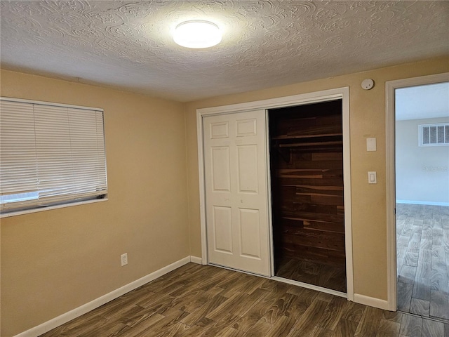 unfurnished bedroom featuring dark hardwood / wood-style flooring, a textured ceiling, and a closet