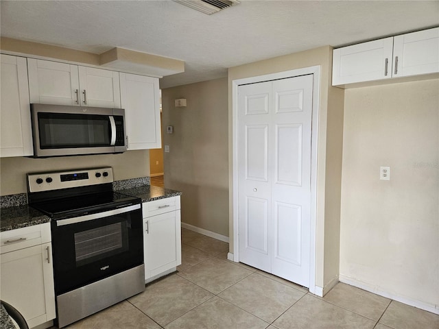 kitchen with white cabinets, light tile patterned flooring, appliances with stainless steel finishes, and dark stone counters