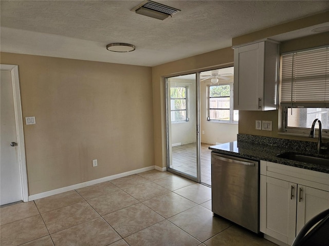 kitchen with dishwasher, sink, light tile patterned floors, dark stone countertops, and white cabinets