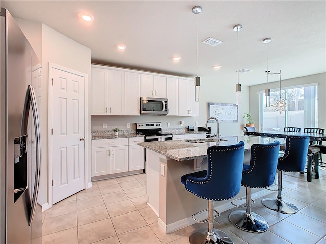 kitchen with a kitchen island with sink, white cabinets, hanging light fixtures, appliances with stainless steel finishes, and a notable chandelier