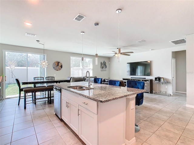 kitchen with light stone countertops, decorative light fixtures, a center island with sink, dishwasher, and white cabinetry