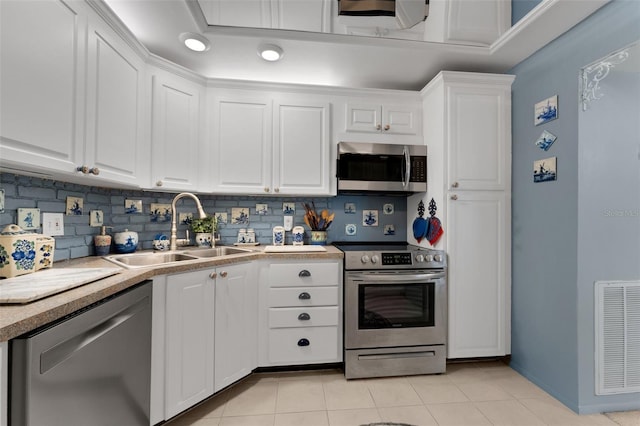 kitchen featuring appliances with stainless steel finishes, tasteful backsplash, sink, light tile patterned floors, and white cabinetry