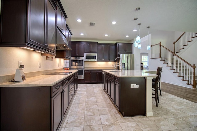 kitchen with a center island with sink, sink, appliances with stainless steel finishes, decorative light fixtures, and dark brown cabinets