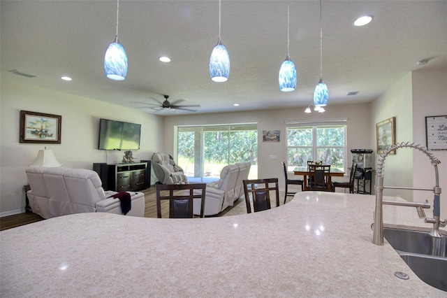 kitchen featuring a textured ceiling, decorative light fixtures, light stone counters, and sink