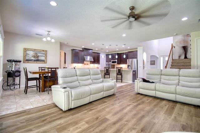 living room with ceiling fan with notable chandelier, light wood-type flooring, and a textured ceiling