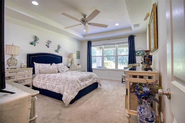 bedroom with light carpet, a textured ceiling, a tray ceiling, and ceiling fan