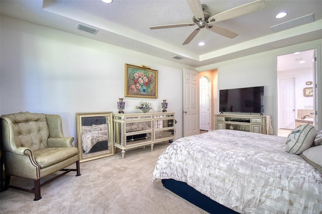 bedroom featuring ceiling fan, a raised ceiling, ensuite bathroom, and light carpet