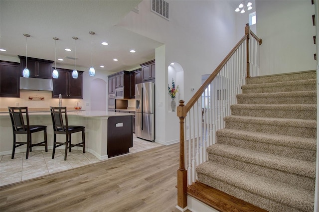 kitchen with a kitchen bar, dark brown cabinetry, stainless steel fridge with ice dispenser, light hardwood / wood-style floors, and a kitchen island