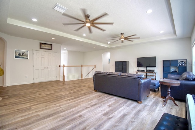 living room with a tray ceiling, ceiling fan, light hardwood / wood-style flooring, and a textured ceiling