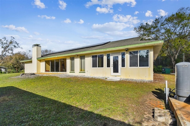 back of property with a yard and solar panels