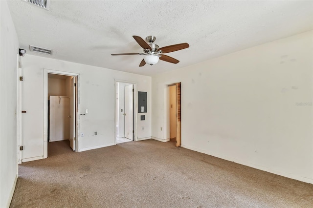 unfurnished bedroom with ceiling fan, electric panel, light colored carpet, a textured ceiling, and a walk in closet