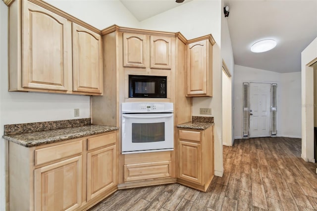 kitchen featuring white oven, dark hardwood / wood-style flooring, dark stone countertops, vaulted ceiling, and light brown cabinetry