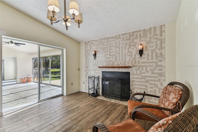 sitting room with a tile fireplace, wood-type flooring, a textured ceiling, vaulted ceiling, and ceiling fan with notable chandelier