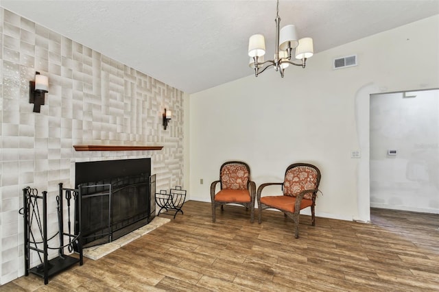 living area featuring a chandelier, vaulted ceiling, a textured ceiling, wood-type flooring, and a fireplace