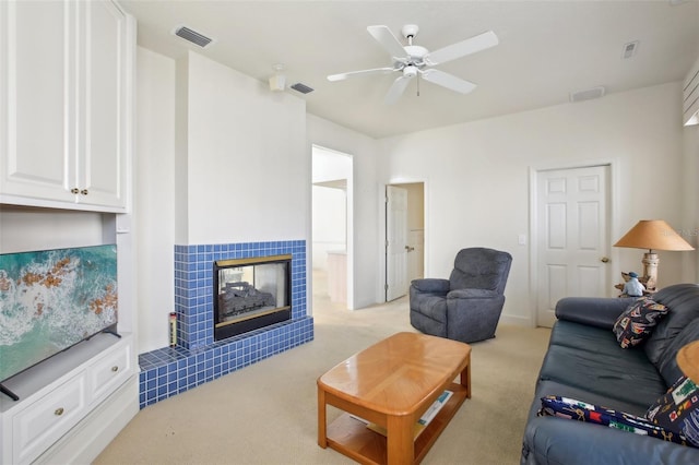 carpeted living room featuring a tiled fireplace and ceiling fan