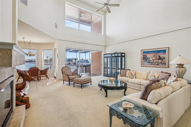 living room with a high end fireplace, a towering ceiling, light colored carpet, ceiling fan, and a water view