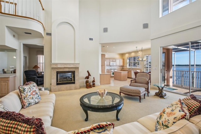 living room with a tile fireplace, a high ceiling, a water view, and plenty of natural light