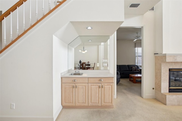 bar featuring light colored carpet, ceiling fan, a tile fireplace, light brown cabinets, and hanging light fixtures