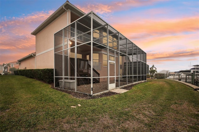 property exterior at dusk featuring a lawn and glass enclosure