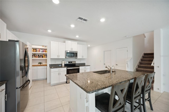 kitchen with appliances with stainless steel finishes, dark stone counters, sink, a center island with sink, and white cabinetry