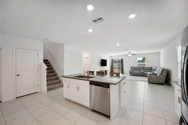 kitchen with stainless steel dishwasher, sink, light tile patterned floors, white cabinetry, and an island with sink