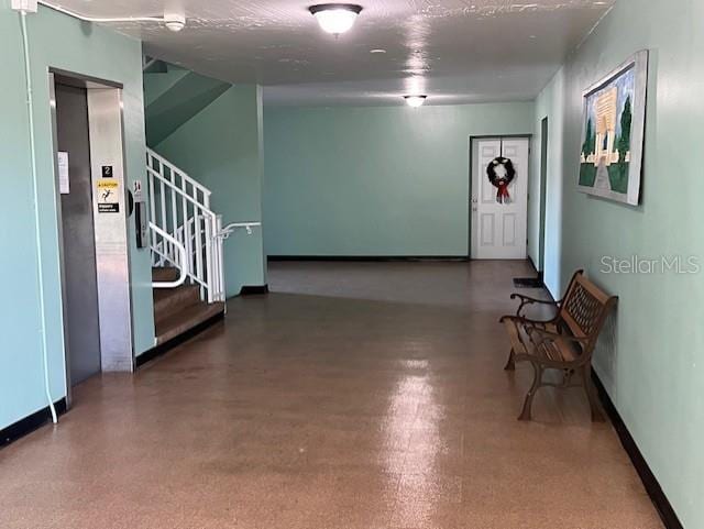 entrance foyer featuring a textured ceiling, stairway, elevator, and baseboards