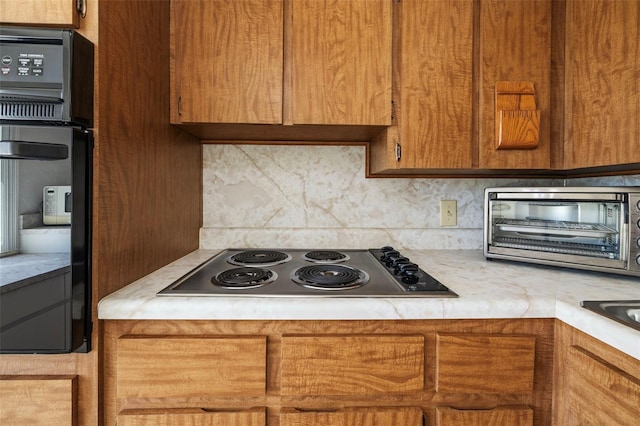 kitchen with a toaster, light countertops, stainless steel electric stovetop, backsplash, and black oven