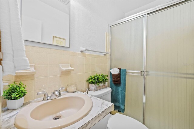 full bathroom featuring a stall shower, vanity, toilet, and tile walls