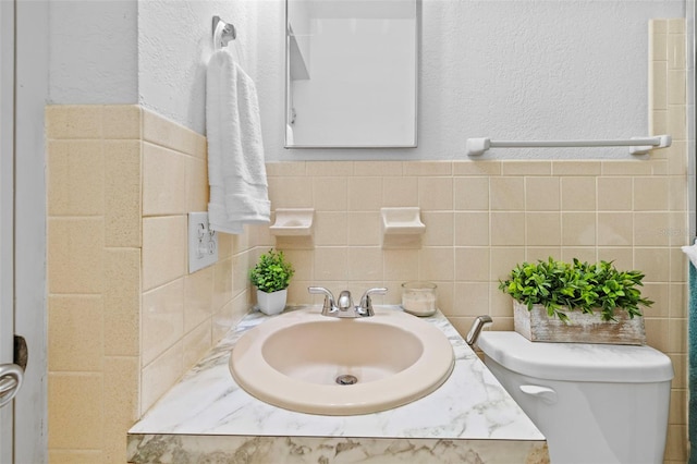 bathroom with toilet, vanity, tile walls, and a textured wall