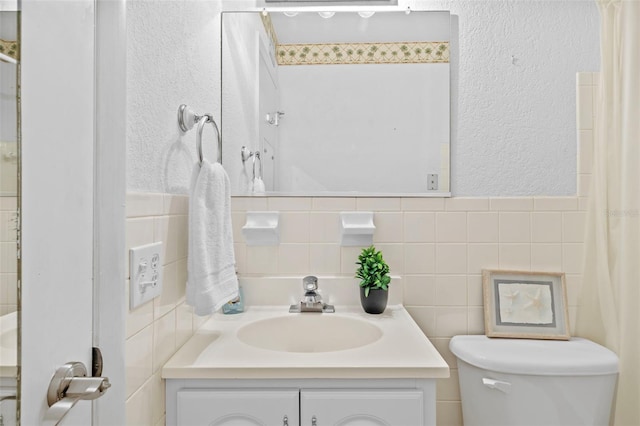 bathroom with a textured wall, tile walls, toilet, and vanity