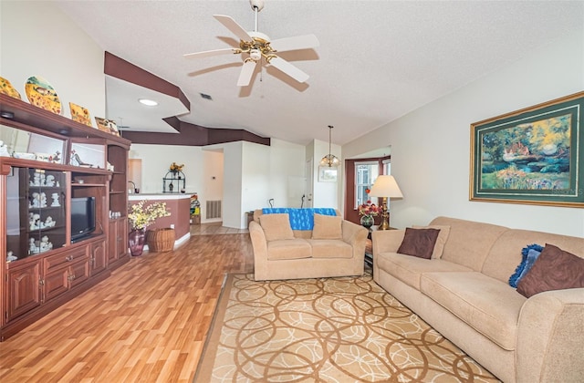 living room with hardwood / wood-style floors, ceiling fan with notable chandelier, a textured ceiling, and vaulted ceiling