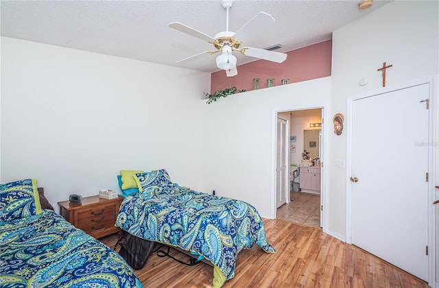 bedroom featuring ceiling fan, ensuite bathroom, a textured ceiling, and light hardwood / wood-style flooring