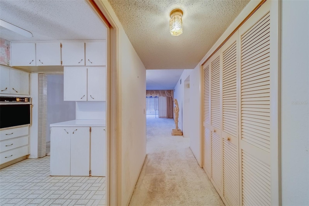 hall featuring light carpet and a textured ceiling