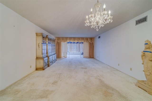 carpeted empty room with a notable chandelier and a textured ceiling