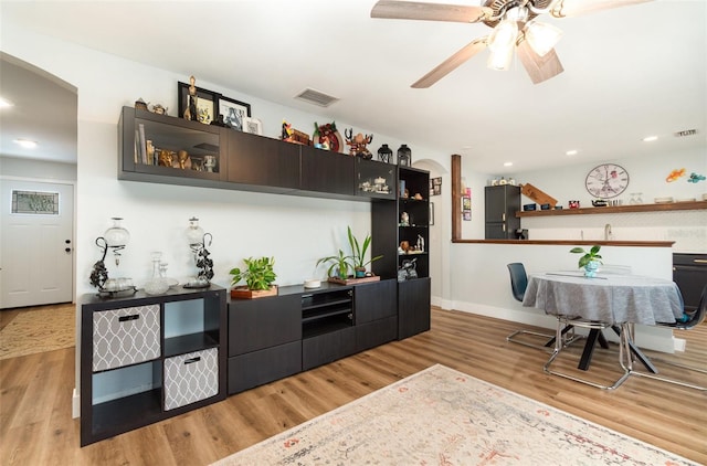 bar with light wood-type flooring, black fridge, and ceiling fan