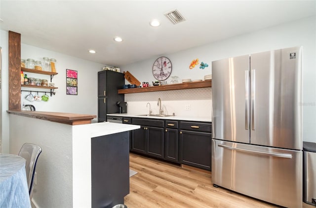 kitchen featuring decorative backsplash, light hardwood / wood-style flooring, stainless steel refrigerator, and sink