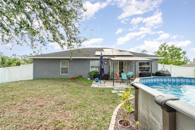 back of house featuring a lawn, a patio, a fenced in pool, and solar panels