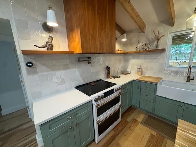 kitchen featuring tasteful backsplash, sink, beam ceiling, light hardwood / wood-style flooring, and high quality range