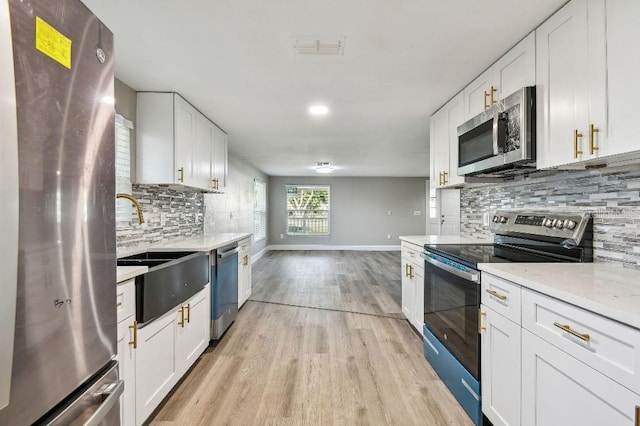 kitchen with white cabinets, sink, appliances with stainless steel finishes, tasteful backsplash, and light hardwood / wood-style floors