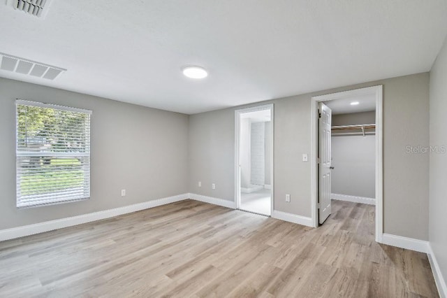 unfurnished bedroom with ensuite bath, a spacious closet, a closet, and light wood-type flooring