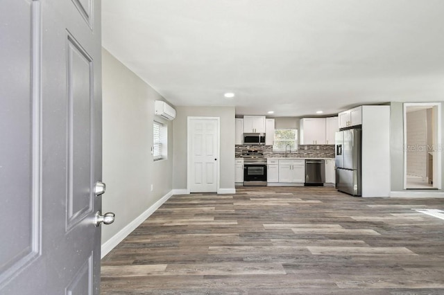 kitchen featuring a wall mounted air conditioner, appliances with stainless steel finishes, backsplash, wood-type flooring, and white cabinetry