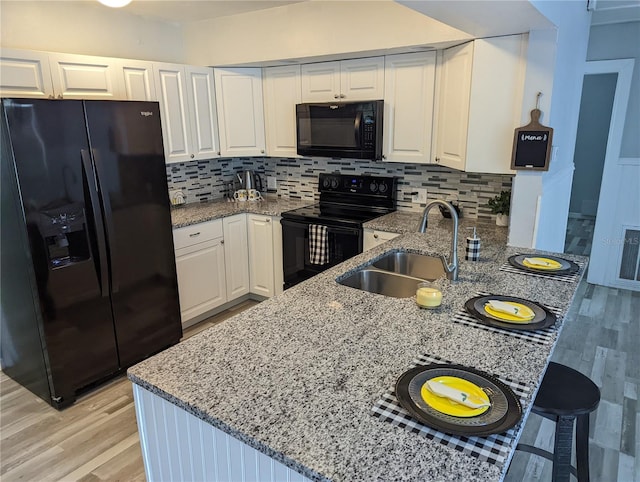 kitchen featuring kitchen peninsula, light stone countertops, sink, black appliances, and white cabinets