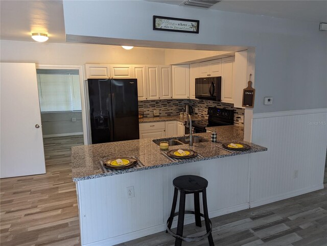 kitchen featuring dark stone counters, kitchen peninsula, white cabinetry, and black appliances