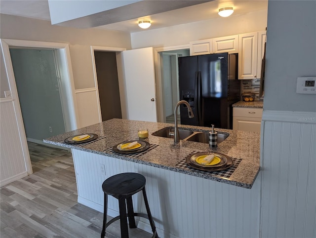 kitchen with white cabinetry, sink, black fridge, dark stone countertops, and a breakfast bar