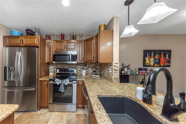 kitchen featuring stainless steel appliances, a sink, backsplash, light stone countertops, and brown cabinetry