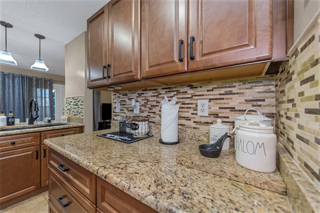 kitchen with sink, light stone counters, backsplash, pendant lighting, and a textured ceiling