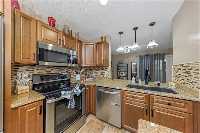 kitchen featuring light stone countertops, sink, kitchen peninsula, decorative light fixtures, and appliances with stainless steel finishes