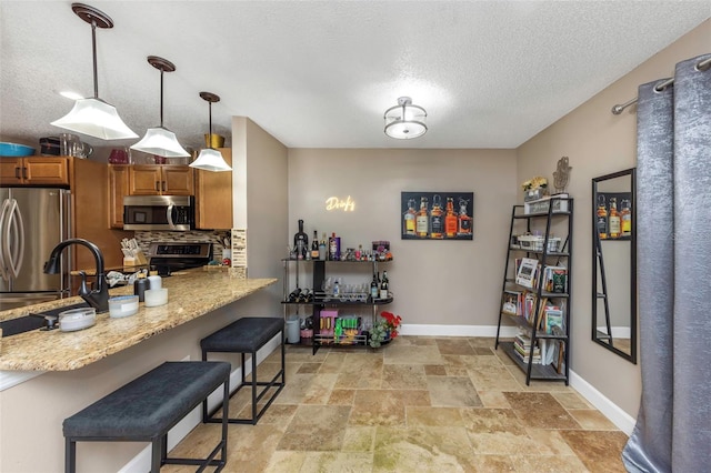 kitchen with kitchen peninsula, appliances with stainless steel finishes, light stone counters, a breakfast bar, and hanging light fixtures